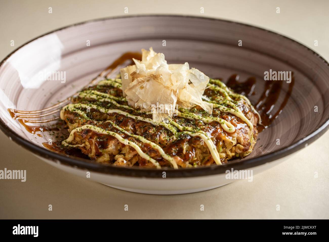 Da sopra di gustoso piatto tradizionale giapponese okonomiyaki con salsa condita con fiocchi di bonito servito in ciotola di ceramica su sfondo chiaro Foto Stock