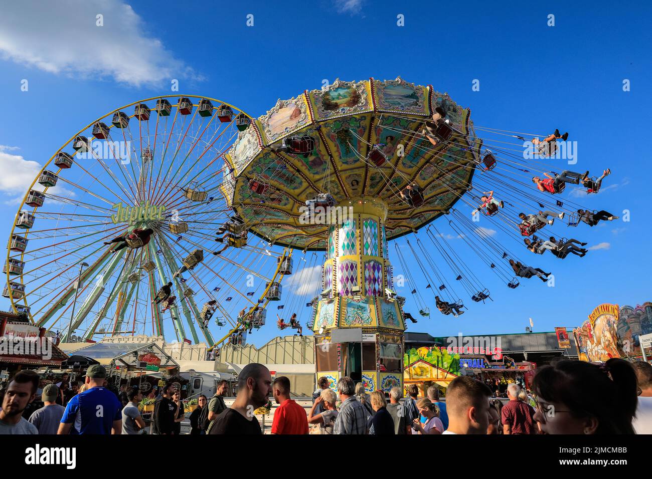 Crange, Herne, NRW, 05th ago, 2022. La gente gode il suo giro su un merry-go-round tradizionale splendidamente decorato sullo sfondo giusto con la ruota di ferro di Giove. Il giorno di apertura ufficiale della Cranger Kirmes del 2022, la più grande fiera del 3rd della Germania e la più grande del suo genere in NRW, vede migliaia di visitatori che si divertono con giostre, montagne russe, birrerie, bancarelle di cibo e altre attrazioni. Credit: Imagplotter/Alamy Live News Foto Stock