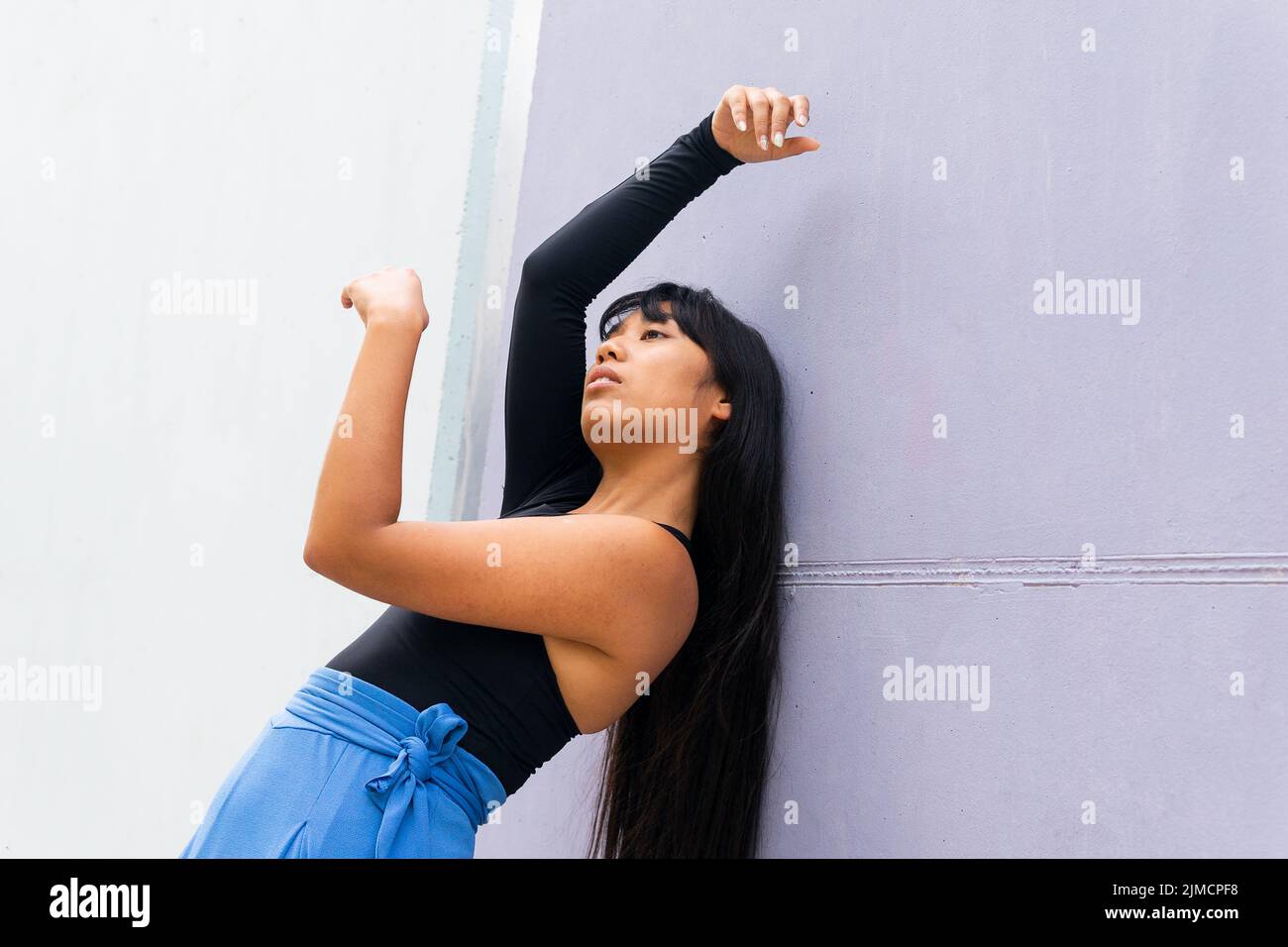 Basso angolo di graziosa giovane donna asiatica che alza le braccia e si piega mentre balla vicino al muro della costruzione sulla strada della città Foto Stock