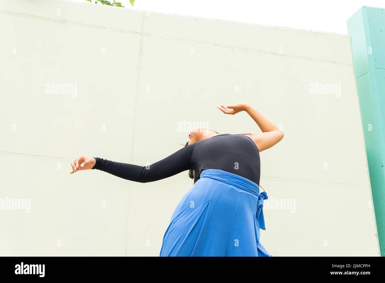 Basso angolo di giovane donna asiatica irriconoscibile che alza le braccia e si piega mentre balla vicino al muro della costruzione sulla strada della città Foto Stock