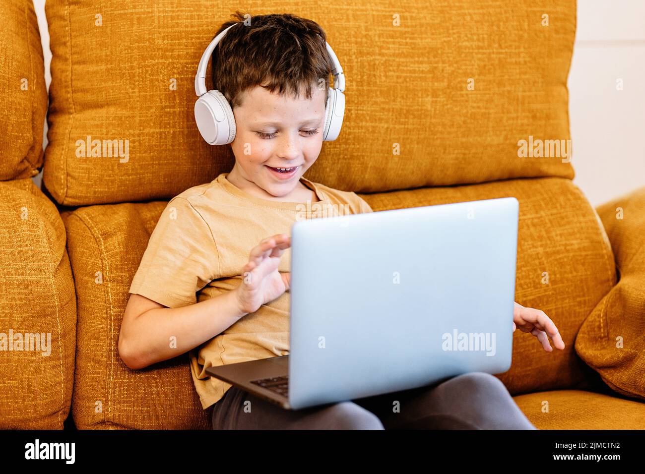 Felice ragazzo seduto su un divano con le cuffie sulla testa e utilizzando  il computer portatile a casa Foto stock - Alamy