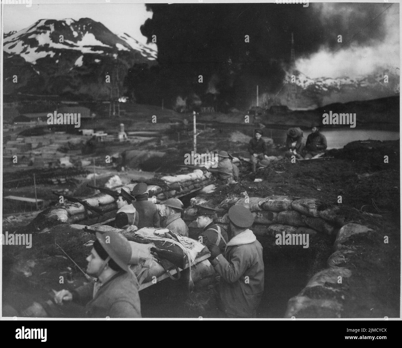 Attacco apanese al Porto Olandese, 3 giugno 1942. Gruppo di Marines sull'allerta tra gli attacchi. Il fumo dai serbatoi di carburante in fiamme sullo sfondo era stato messo in fiamme da un bombardiere da immersione il giorno precedente. Foto Stock