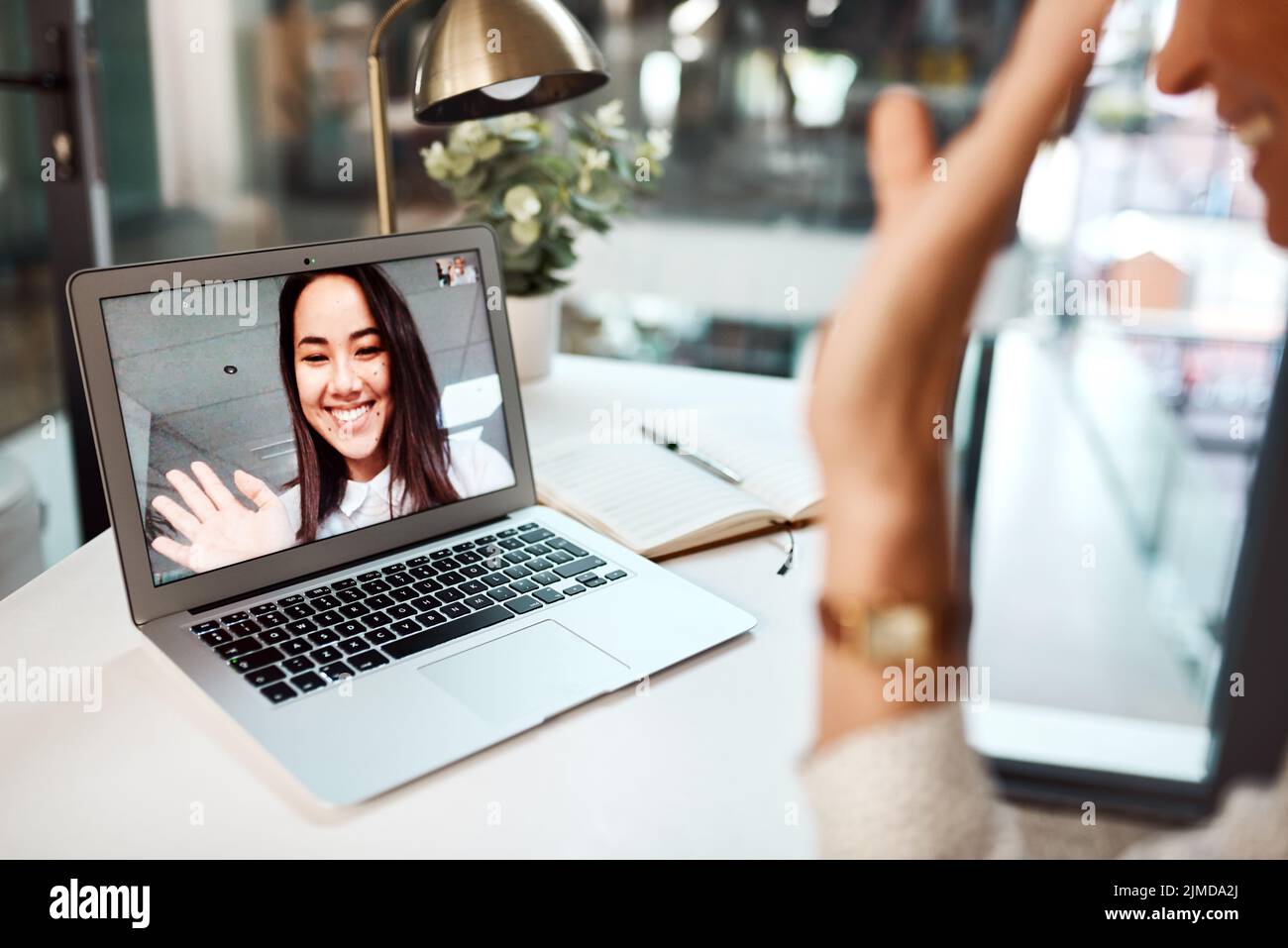 Le collaborazioni digitali si sono svolte con facilità in reparti e luoghi diversi. Una giovane donna che sventolava mentre compare sullo schermo di un notebook durante una videochiamata. Foto Stock