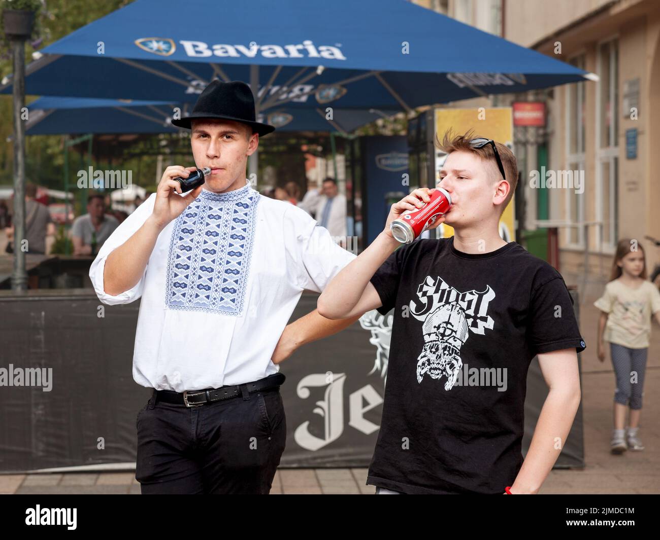 Foto di due giovani, slovacchi, che indossano un costume tradizionale slovacco a Kovacica, Serbia bevendo alcol e fumando sigarette elettroniche Foto Stock