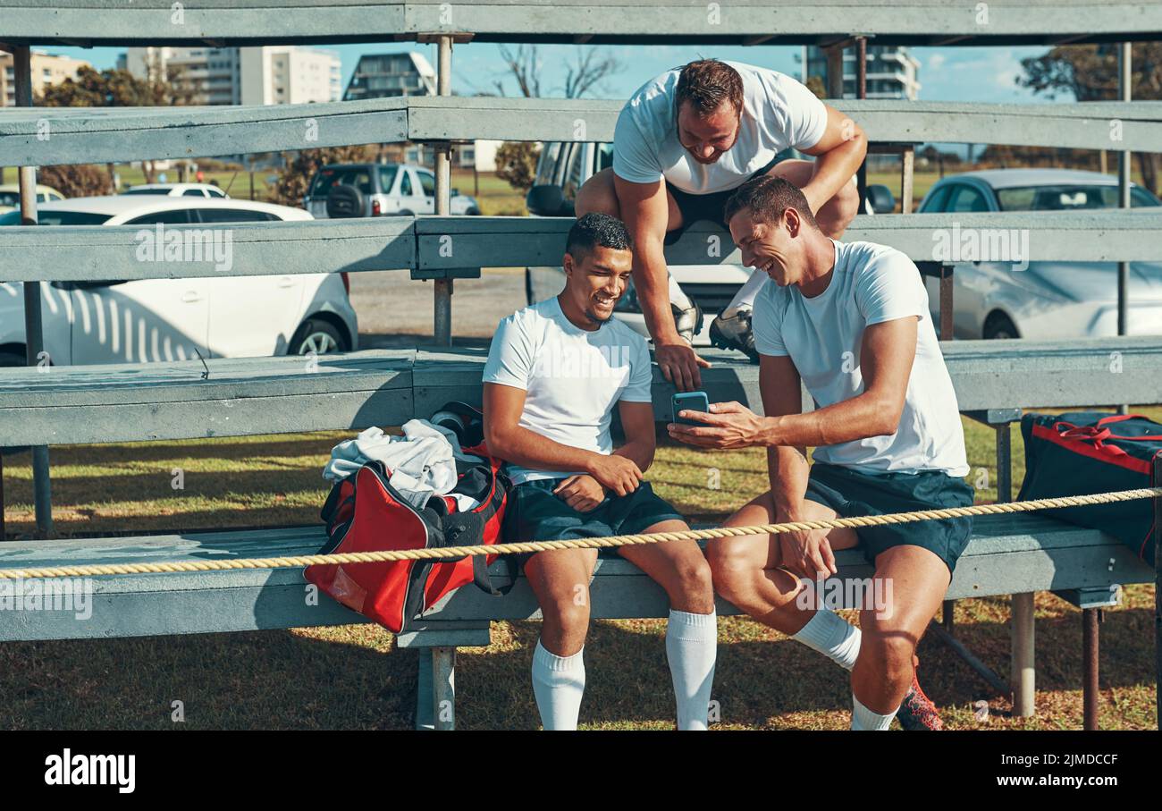 Impara a divertirti con il gioco e le persone che ti circondano. Un giocatore di rugby che mostra ai compagni di squadra qualcosa sul suo cellulare. Foto Stock