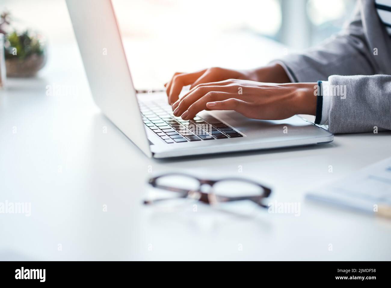 Primo piano di mani di una persona d'affari che digita su un laptop, che naviga in internet online e che conclude una proposta mentre si siede a un tavolo in un ufficio Foto Stock