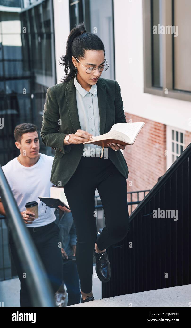 Lenta e stabile vince la gara d'affari. Una giovane donna d'affari che guarda il suo notebook mentre cammina sulle scale in un ambiente di lavoro moderno. Foto Stock