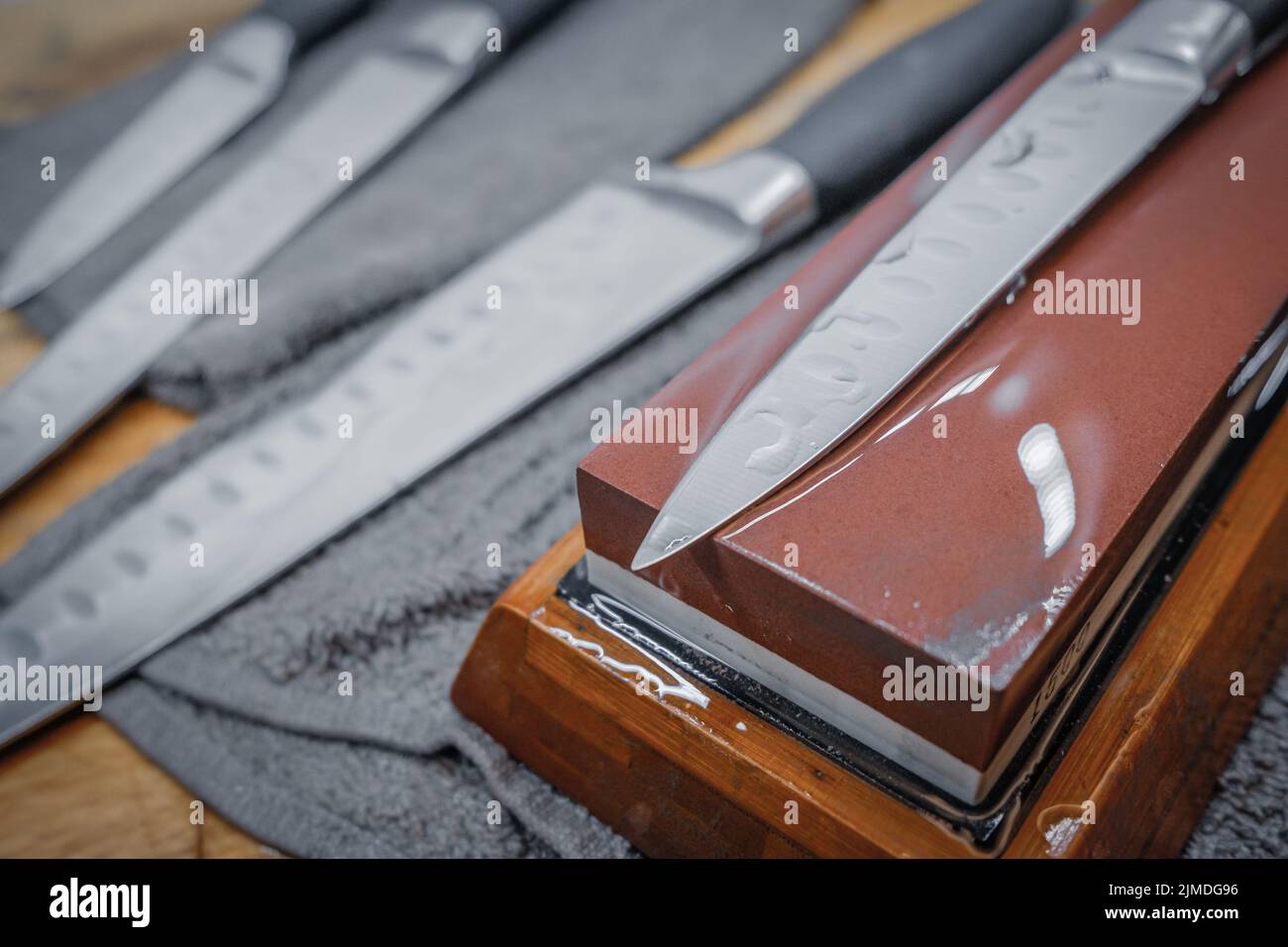 Focalizzazione selettiva sulla lama di un coltello da cucina in acciaio sdraiato su una pietra ad acqua Foto Stock