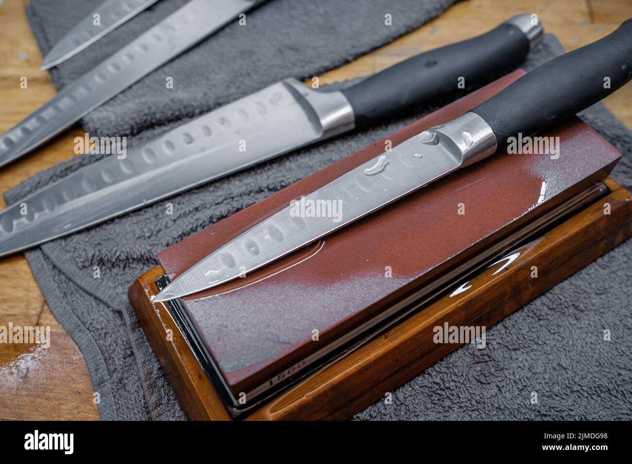 Focalizzazione selettiva sulla lama di un coltello da cucina in acciaio sdraiato su una pietra ad acqua Foto Stock