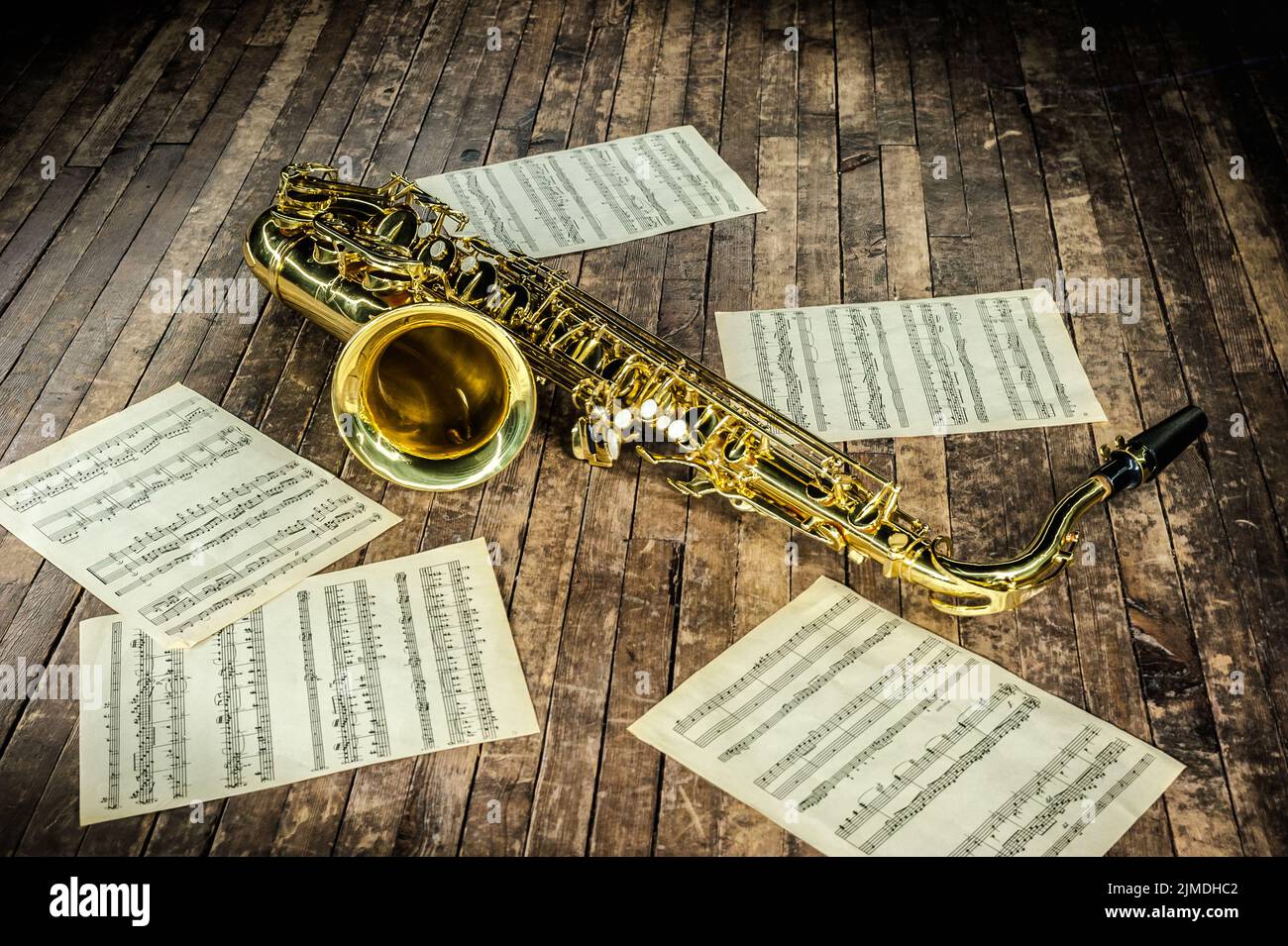 Bellissimo sassofono giallo e carta con note musicali spartiti giacenti su un palco in legno d'epoca Foto Stock