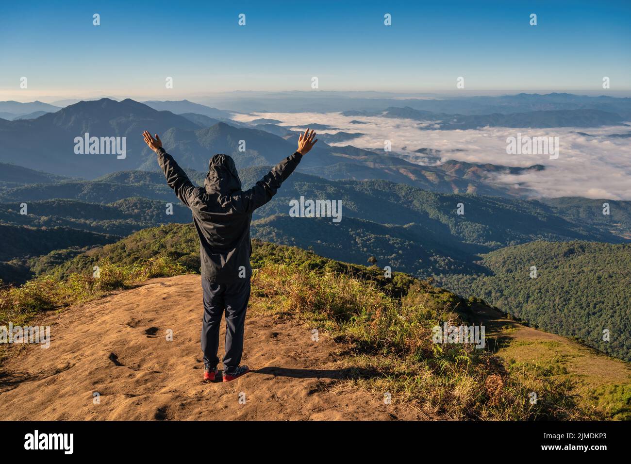 Uomo trekking sollevare mano godere di successo e guardare la catena montuosa in cima alla montagna in tropicale Foto Stock