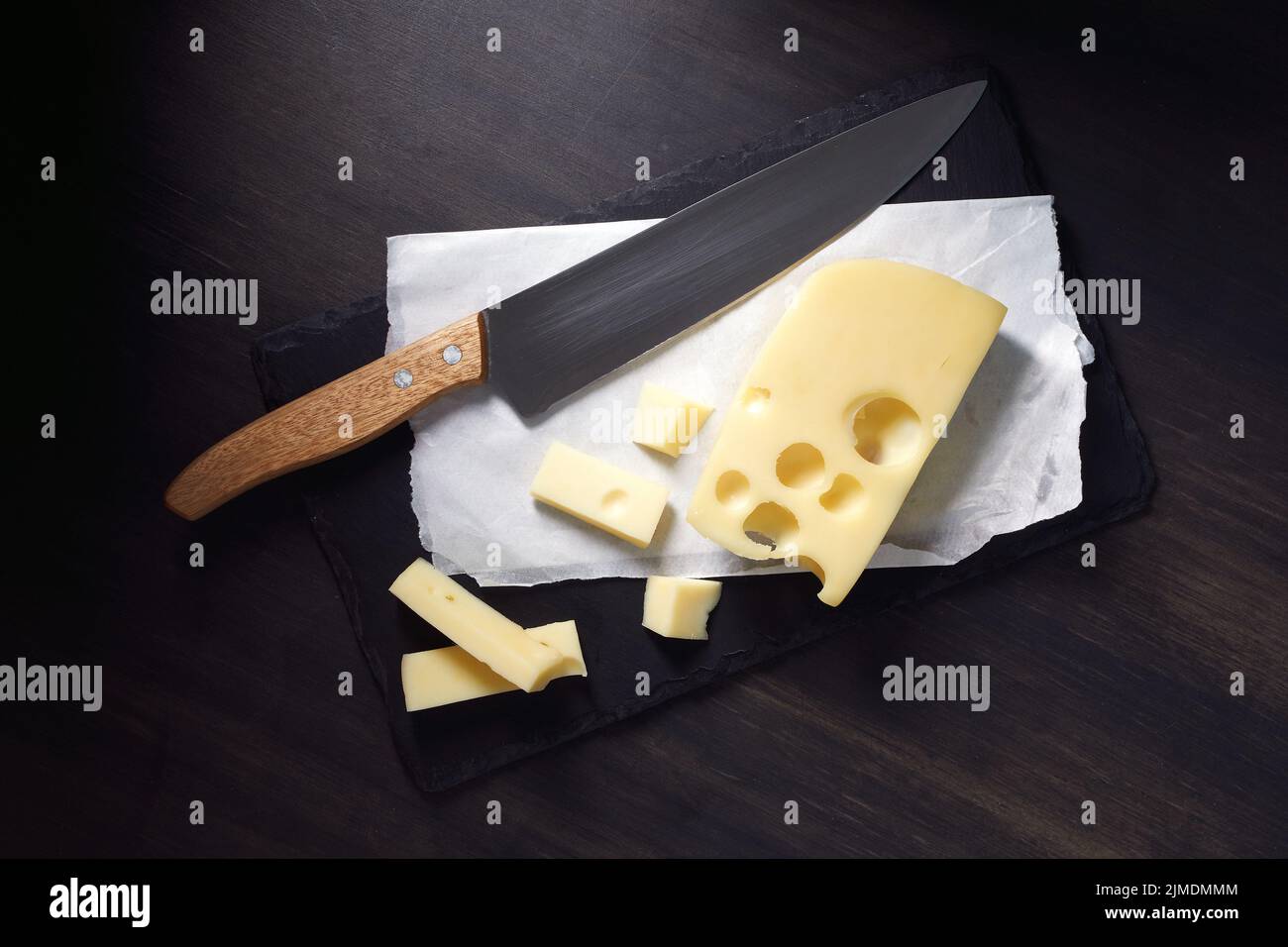 Formaggio Maasdam fresco con buchi e coltello su sfondo scuro Foto Stock
