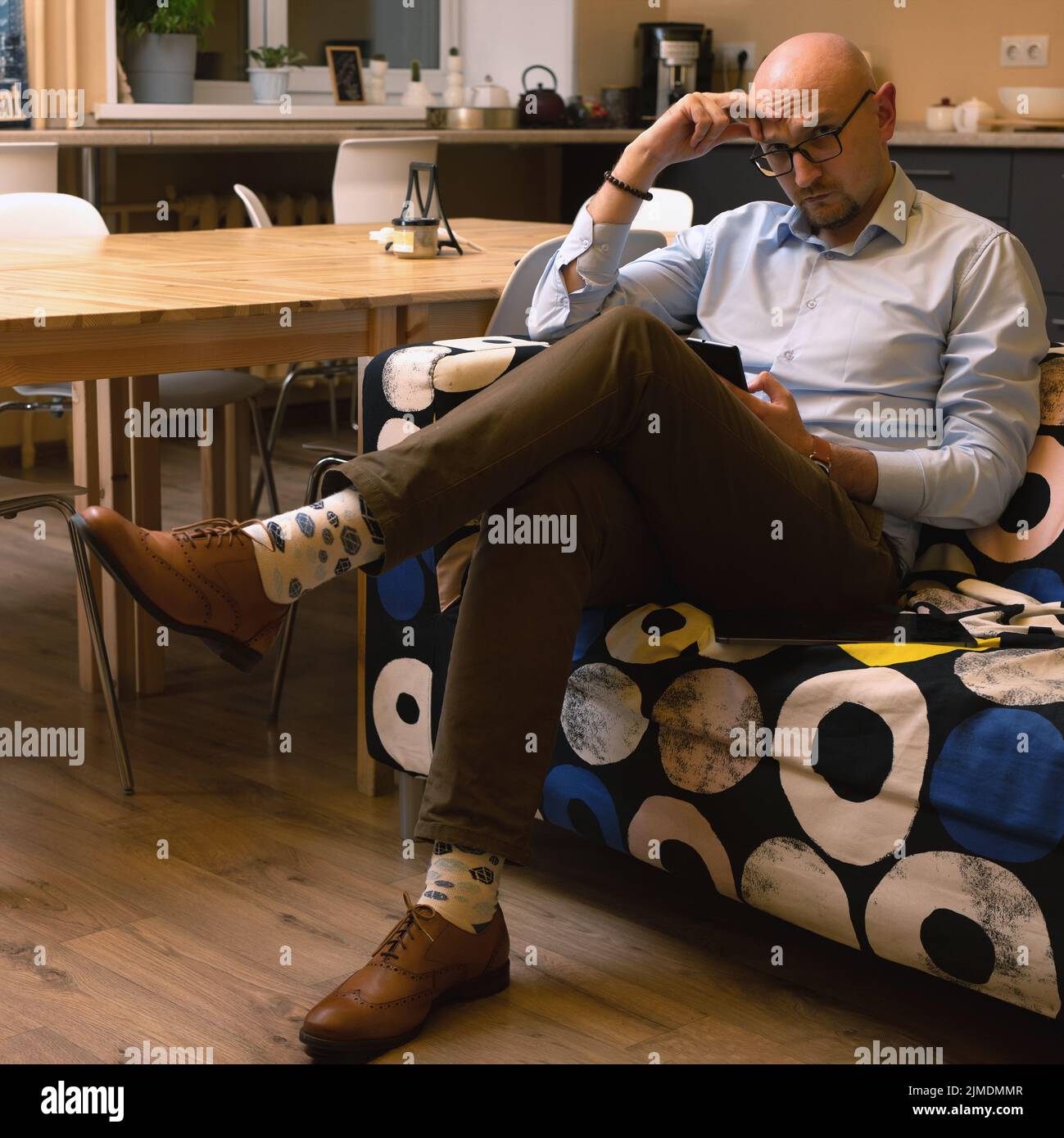 Uomo calvo in occhiali che tiene lo smartphone seduto sul divano in camera. Impostazione Home Office Foto Stock