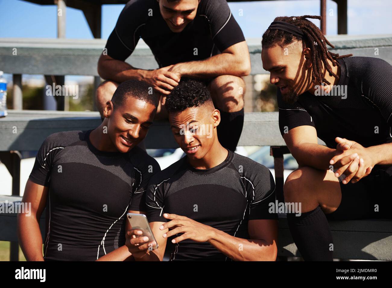 Dai un'occhiata ad alcuni dei momenti salienti del gioco: Un giovane che usa uno smartphone in una partita di rugby circondata dai suoi compagni di squadra. Foto Stock