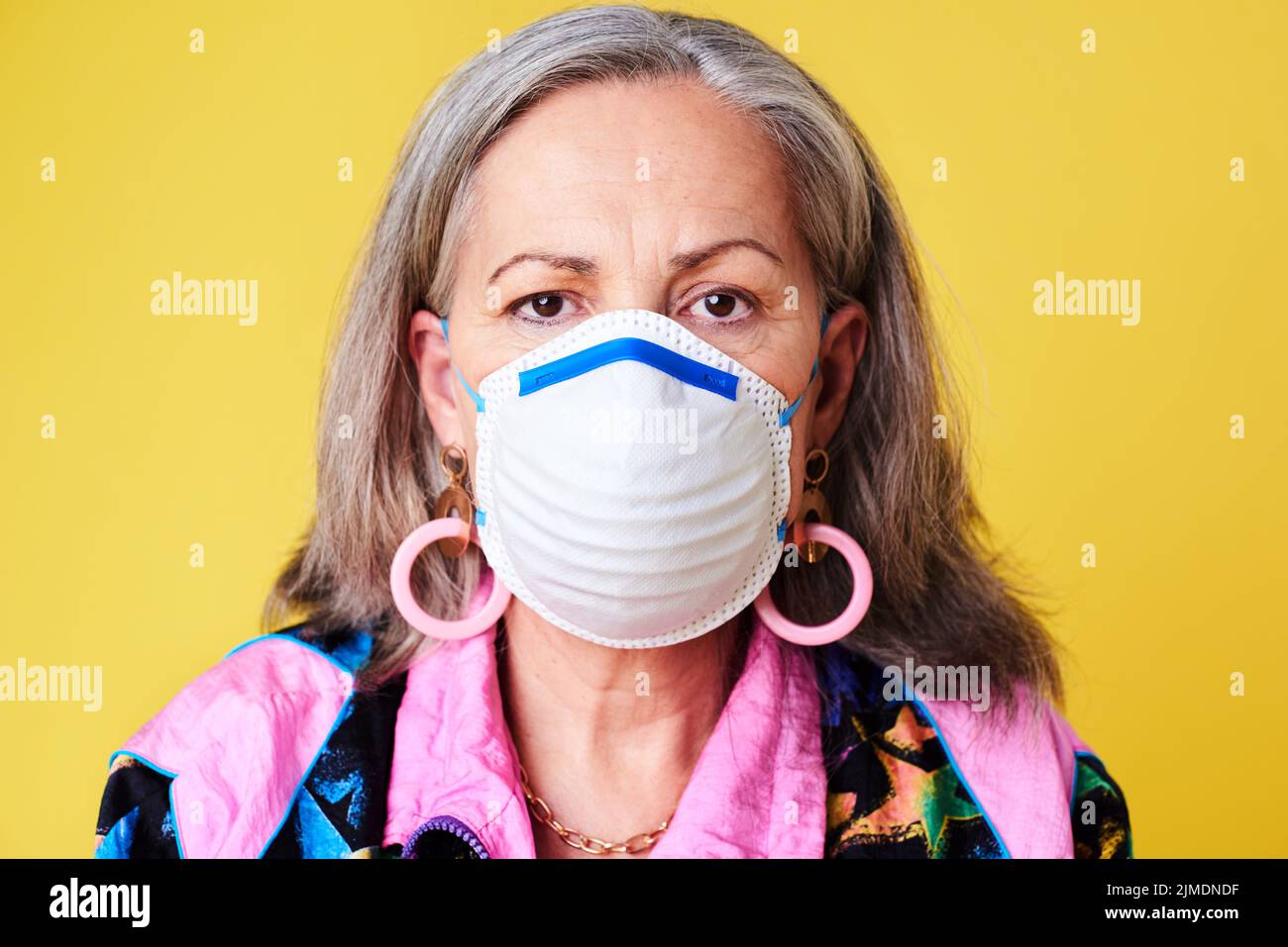 Proteggi i tuoi anni d'oro a tutti i costi. Ritratto di una donna anziana stravagante che indossa una maschera facciale N95 su sfondo giallo. Foto Stock