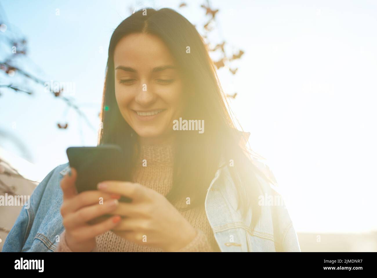 Donna felice che SMS dal suo smartphone in una bella luce del sole Foto Stock