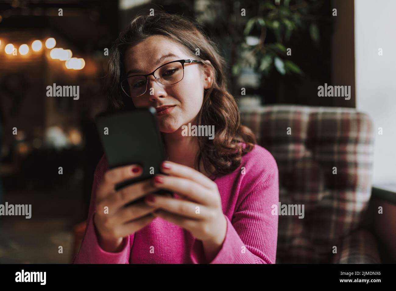 Una donna giovane e graziosa utilizza lo smartphone in interni Foto Stock