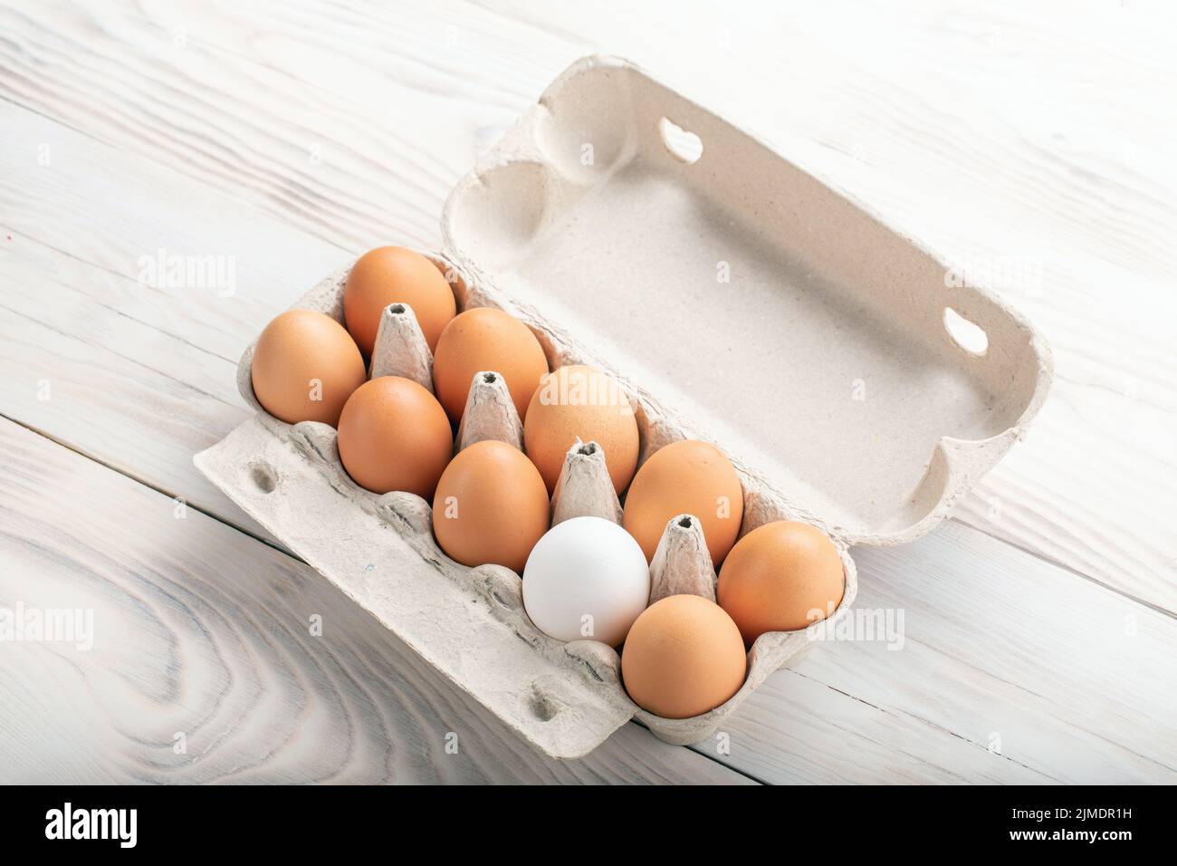 Uova rosolate e tra loro un uovo bianco in scatola di cartone. Concetto di differenza, dissimilarità, sconosciuto. Spazio per il testo Foto Stock