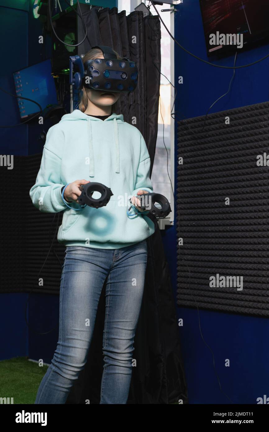 Ragazza adolescente in realtà virtuale casco cerca di controllare il gioco utilizzando i controller nel club VR Foto Stock