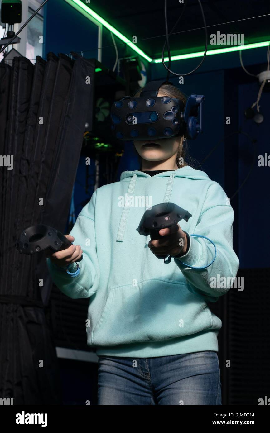 Ragazza con visore per realtà virtuale che utilizza il joystick mentre gioca a un videogioco nel club di gioco vr. Foto Stock