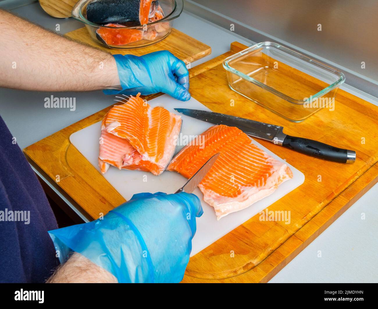 Le mani del cuoco separano i filetti di salmone dalle ossa con un coltello. Foto Stock