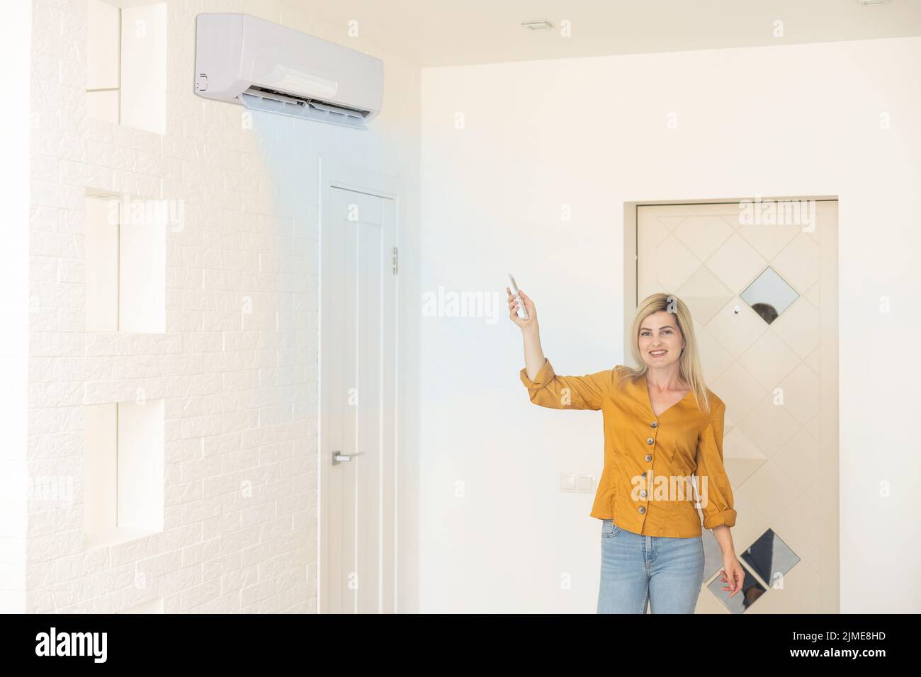 Donna che tiene il telecomando rivolto al condizionatore d'aria Foto Stock