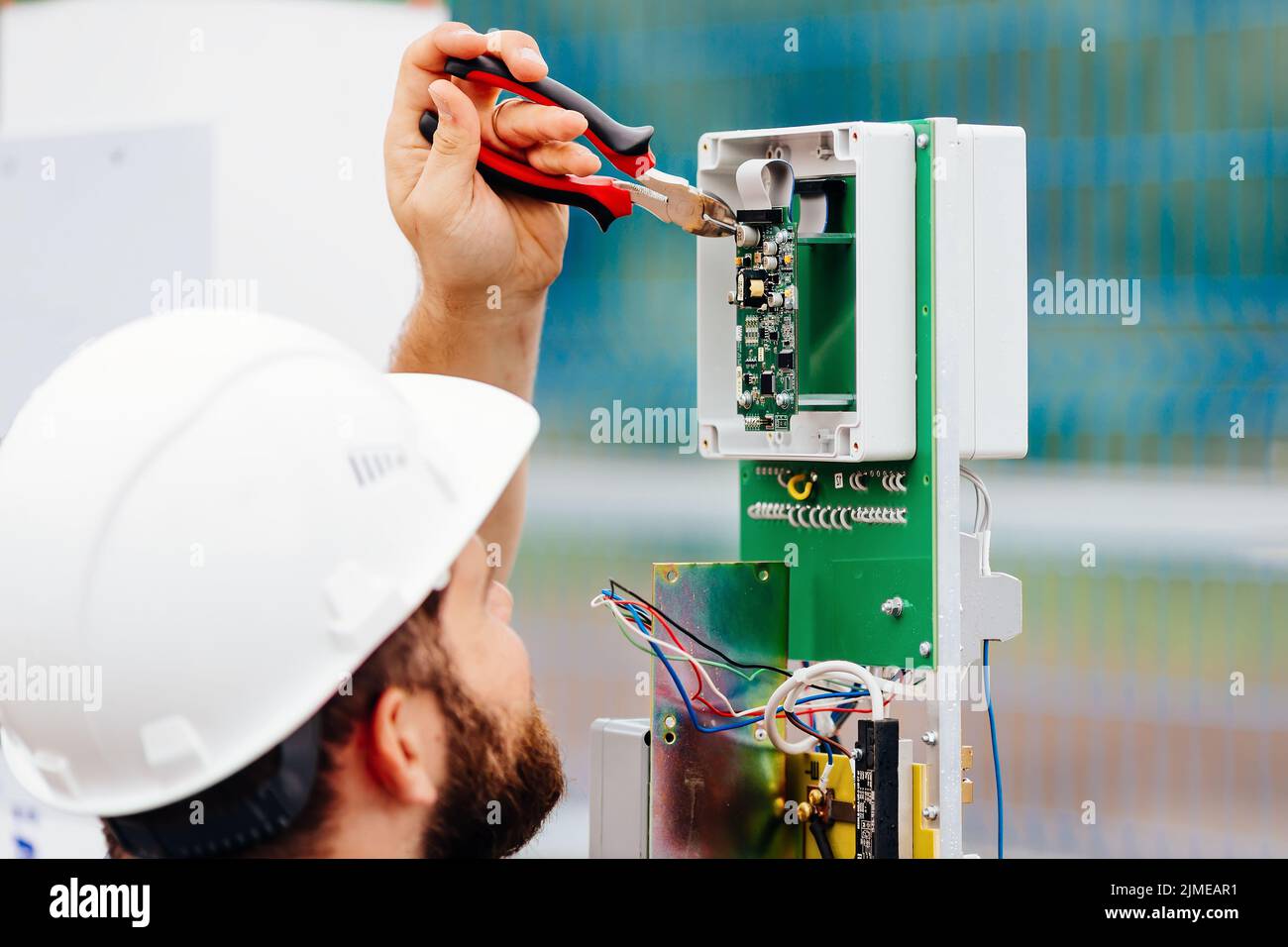 Un ingegnere elettrico qualificato crea un dispositivo di controllo e misurazione in un impianto industriale in una giornata estiva. Foto Stock