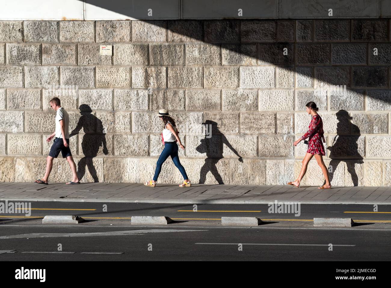 Persone che camminano in fila seguite dalle loro ombre sul muro Foto Stock
