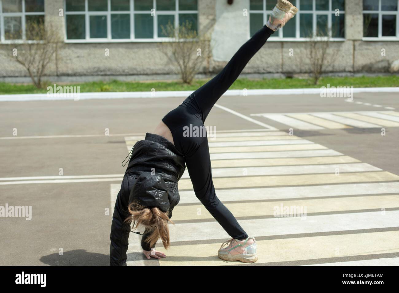 La ragazza mostra acrobatica acrobatica stunt su strada. Il bambino fa la ruota su asfalto. Movimento espressivo. Ginnastica per la salute. Stile di vita attivo. Foto Stock