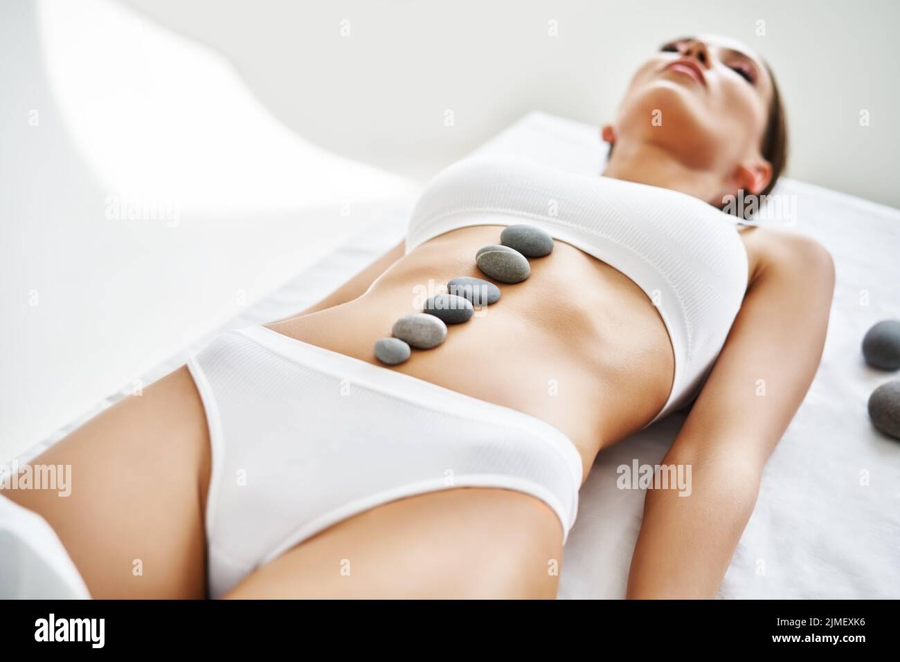 La giovane donna si rilassa sdraiata sul lettino massaggiante con pietre termali sull'addome. Foto Stock