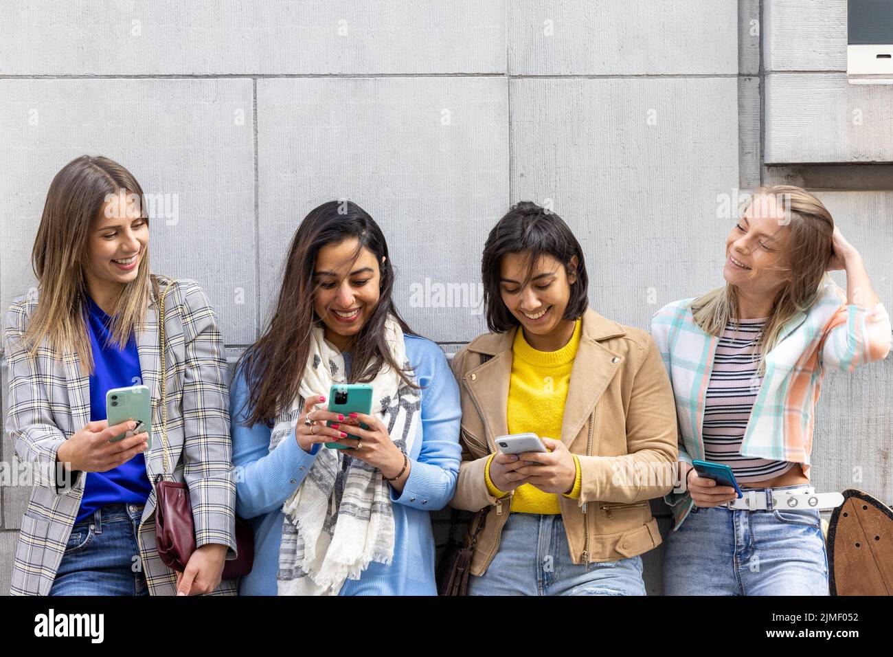 Il gruppo multirazziale di adolescenti si diverte a giocare felicemente con gli smartphone. Utilizzo da parte dei millennial di telefoni cellulari e applicazioni social Foto Stock