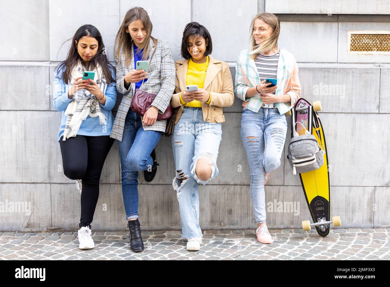 Il gruppo multirazziale di adolescenti si diverte a giocare felicemente con gli smartphone. Utilizzo da parte dei millennial di telefoni cellulari e applicazioni social Foto Stock