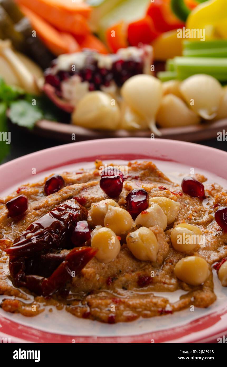 Vista dall'angolo basso sul piatto di hummus vegetale con pomodoro essiccato al sole e ricoperto di ceci e olio d'oliva Foto Stock