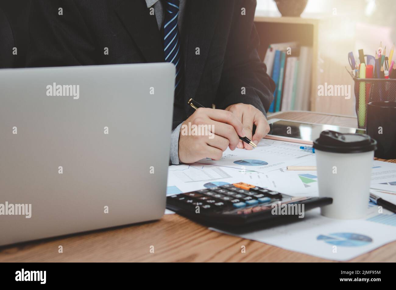 Businessman che tiene la penna documento grafico contabilità finanza carta lavoro analisi grafico di marketing investimenti e rapporto economia con computer portatile su de Foto Stock