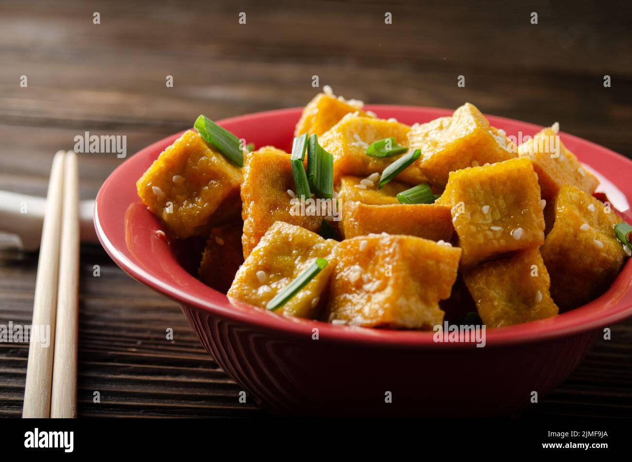 Croccanti e profondi, soffritti i cubetti di tofu fritti con erba cipollina su un tavolo da cucina in legno Foto Stock