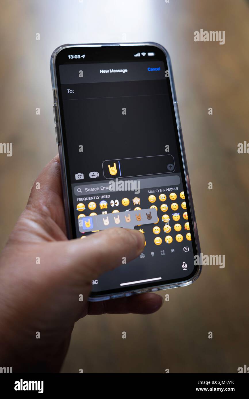 IPhone 13 pro max è tenuto con una mano caucasica che texting un rock dita emoji Foto Stock