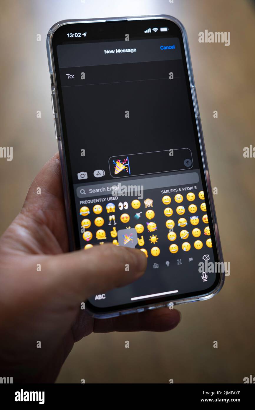 IPhone 13 pro max è tenuto con una mano caucasica che texting un emoji Foto Stock