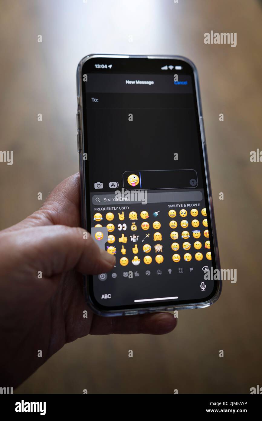 IPhone 13 pro max è tenuto con una mano caucasica che texting un emoji Foto Stock