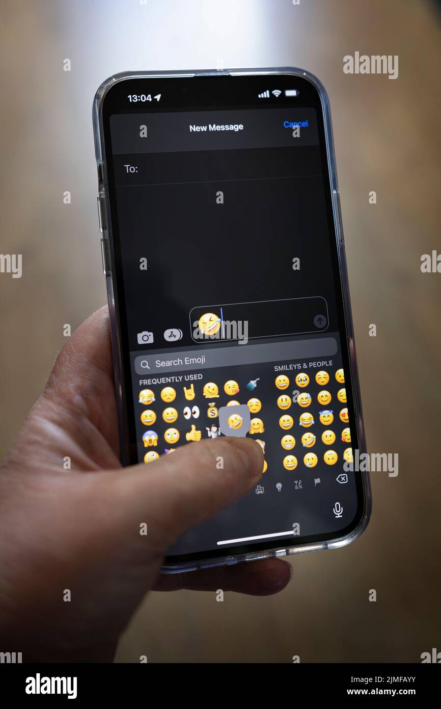 IPhone 13 pro max è tenuto con una mano caucasica che texting un pianto con emotji risate Foto Stock