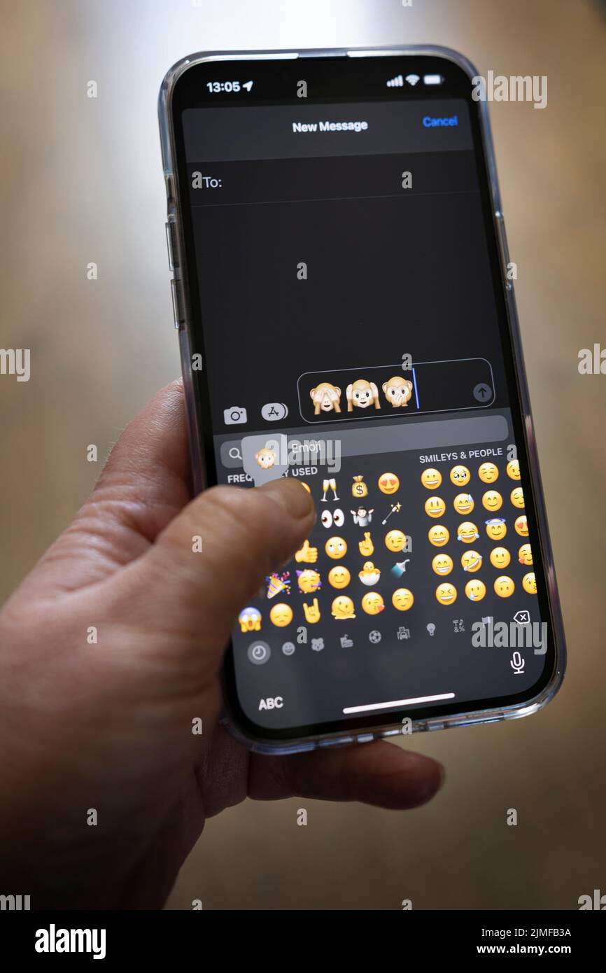 IPhone 13 pro max è tenuto con una mano caucasica che texting le tre scimmie saggio emoji Foto Stock