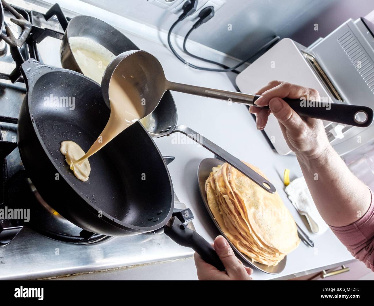 Pastellate versando fuori da un secchio di metallo su una padella unta rossa. Il processo di cottura frittelle. Foto Stock