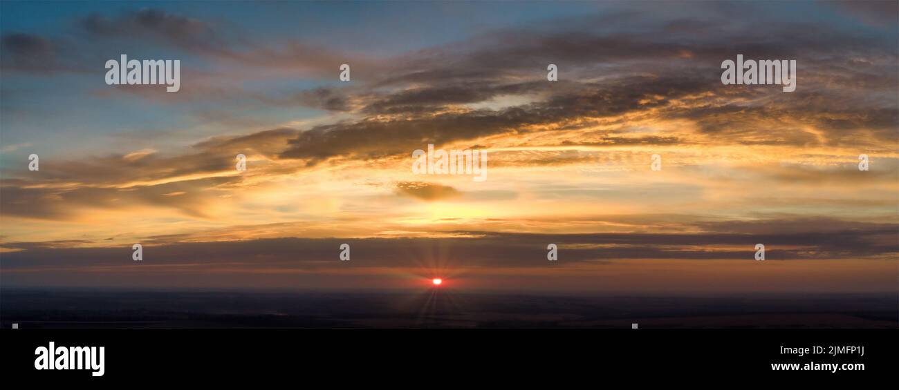 Panorama dell'alba con raggi rossi da dietro le nuvole. Cielo sfocato e nuvole arancioni astratte. Foto Stock