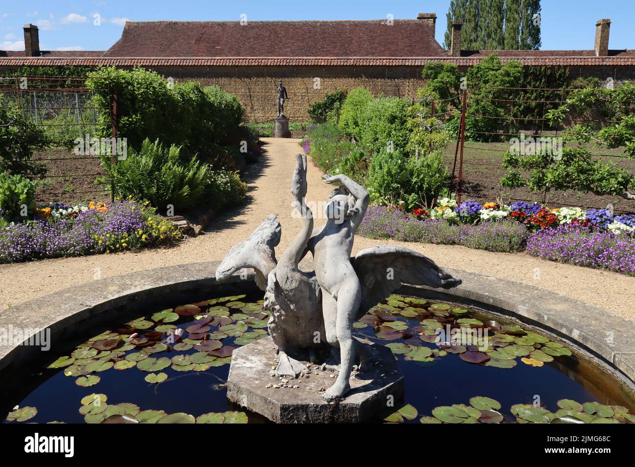 Statua di una ragazza e un cigno in un laghetto di giglio nel giardino murato di una vecchia casa padronale inglese Foto Stock