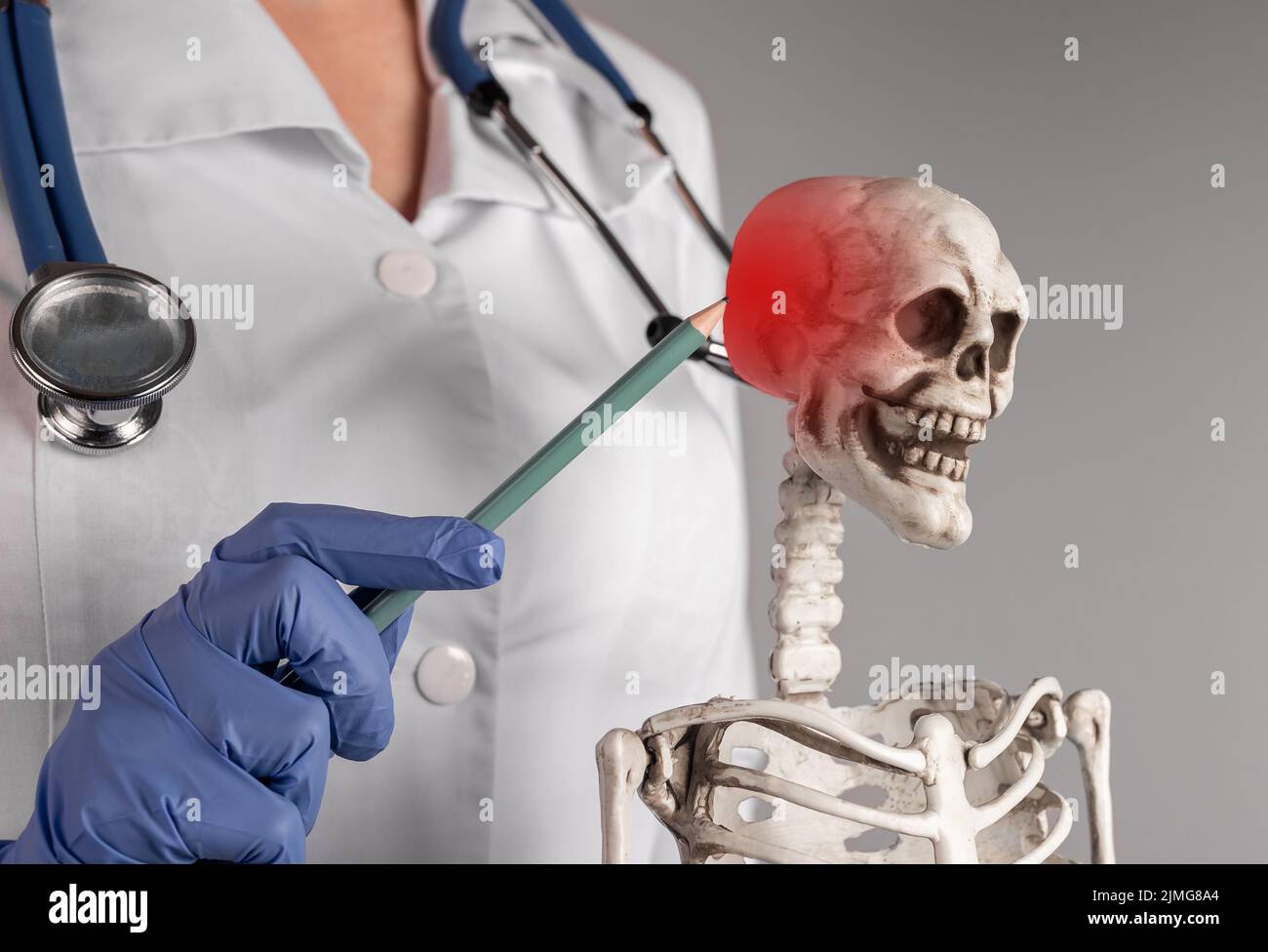 Mano del medico che punta con la matita al cranio dello scheletro con il punto rosso. Nevralgia, cefalea. Anatomia del sistema scheletrico, concetto di educazione medica. Donna in l Foto Stock