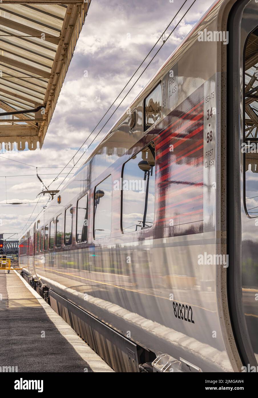 Un carro ferroviario poggia accanto a una piattaforma mentre si prepara a partire. Una tettoia storica è sovratesta e un indicatore luminoso è in distanza. Foto Stock