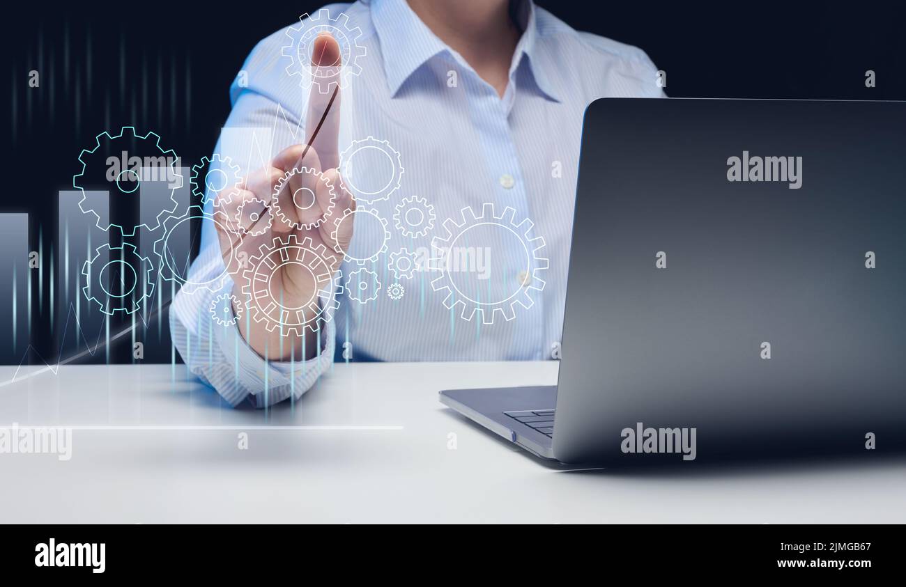 Una donna siede a un notebook e gli ingranaggi virtuali sullo sfondo del grafico. Il concetto di lavoro di squadra efficace, strategia di affari Foto Stock