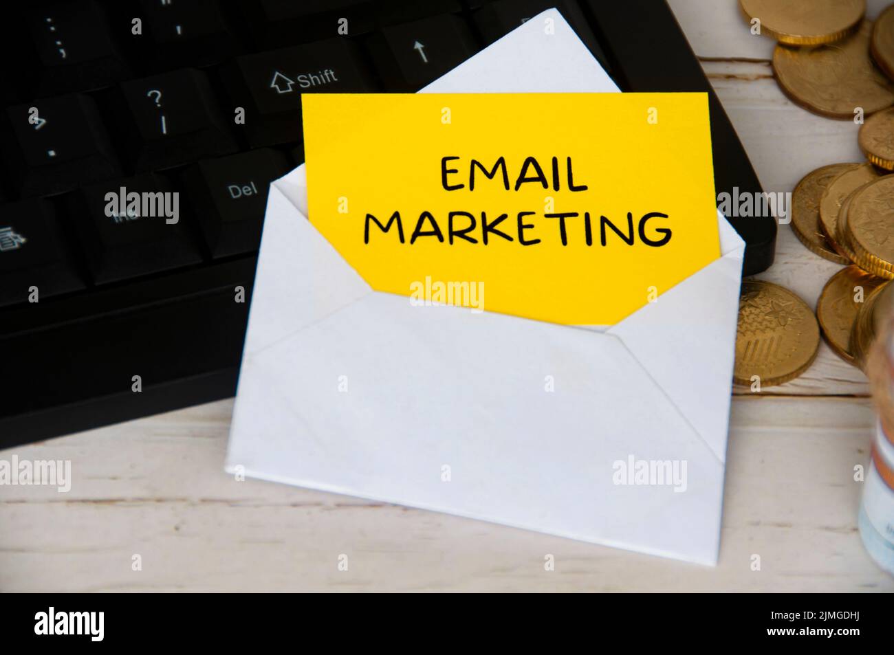 E-mail marketing testo su blocco note giallo in una busta su computer tastiera con monete d'oro. Concetto di business online Foto Stock