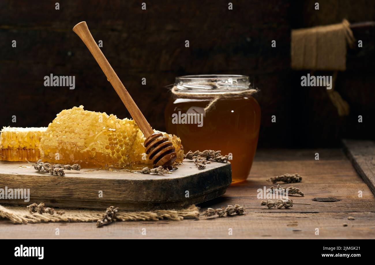 Cera a nido d'ape con miele su un asse di legno, dietro un vaso di miele Foto Stock
