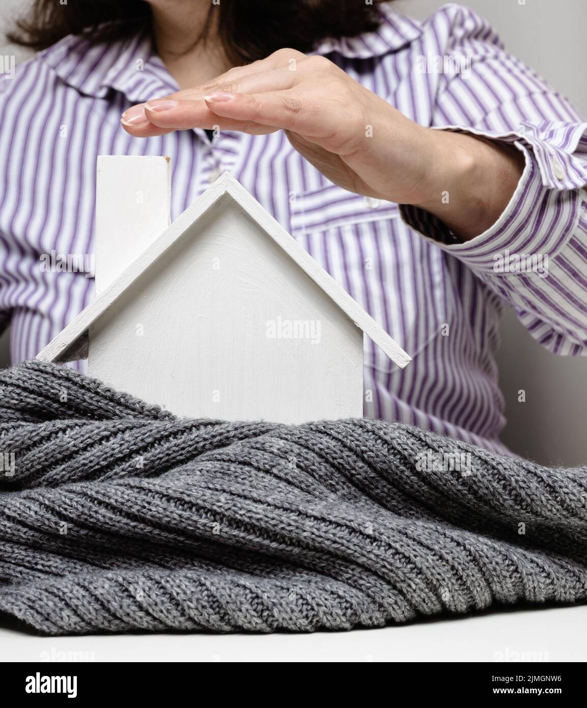Mano femmina su una casa bianca in miniatura avvolta in una sciarpa grigia, concetto di isolamento edilizio Foto Stock