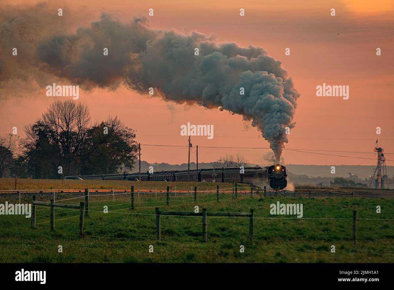 Vista di un treno passeggeri a vapore antico che si avvicina all'alba con un pieno di vapore e fumo Foto Stock